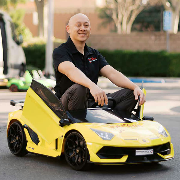 Thomas, the owner of Little Racers OC, smiling as he sits in one of the yellow branded kid-size Lamborghinis